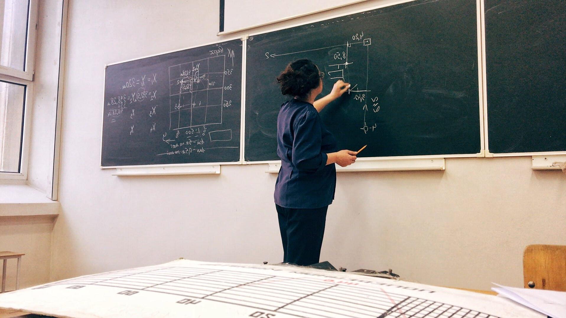 一位女士站在黑板前，用粉笔在黑板上写下一个数学公式